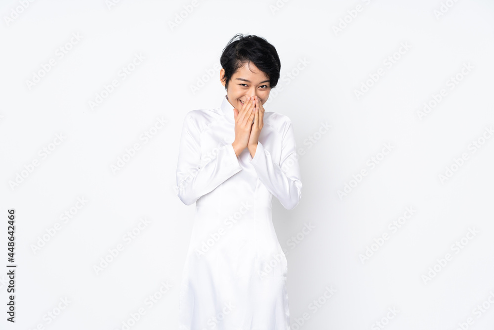 Young Vietnamese woman with short hair wearing a traditional dress over isolated white background happy and smiling covering mouth with hands Young Vietnamese woman with short hair wearing a traditional dress over isolated white background happy and smiling covering mouth with hands