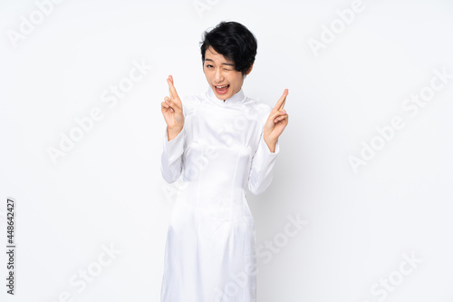 Young Vietnamese woman with short hair wearing a traditional dress over isolated white background with fingers crossing