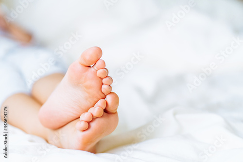 Close up barefoot baby feet lying on white bed linen. Fabric softener, cleanliness. Space for message