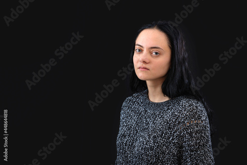 portrait of young woman with long dark hair wearing gray knitted sweater over black background