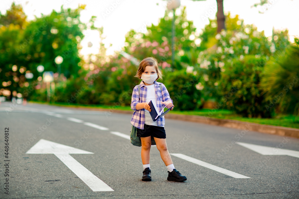 a beautiful little girl, a schoolgirl, is standing on the road, with a backpack, holding a diary in her hands a beautiful little girl, a schoolgirl, is standing on the road, with a backpack, holding a diary in her hands