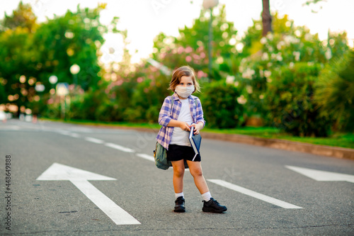 a beautiful little girl, a schoolgirl, is standing on the road, with a backpack, holding a diary in her hands