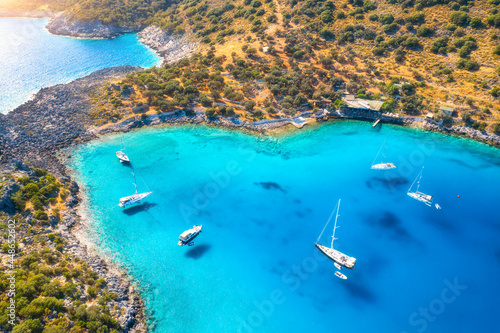 Fototapeta Naklejka Na Ścianę i Meble -  Aerial view of beautiful yachts and boats on the sea at sunset in summer. Akvaryum koyu in Turkey. Top view of luxury yachts, sailboats, clear blue water, rock, lagoon, mountain, green trees. Travel