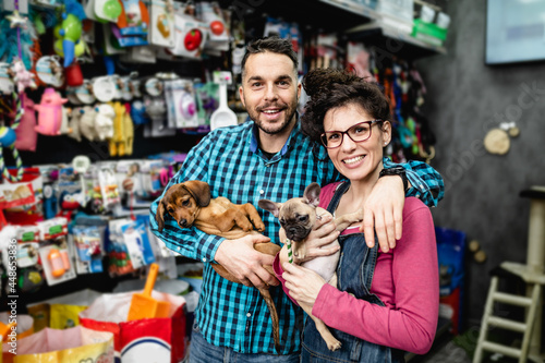 Happy couple with their puppies buying toys and food in pet shop.