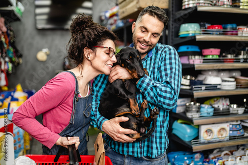 Happy couple buying toys and food for their Dachshund in pet shop.