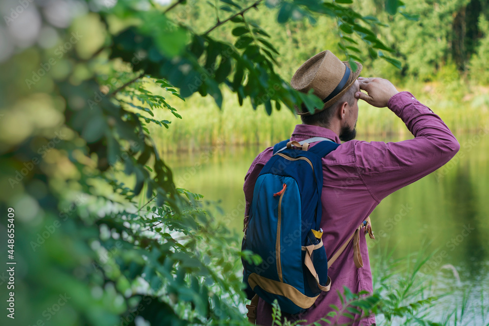 A tourist man stands on the shore of the lake with a backpack for travel. Concept on the topic of tourism. A tourist man stands on the shore of the lake with a backpack for travel. Concept on the topic of tourism.