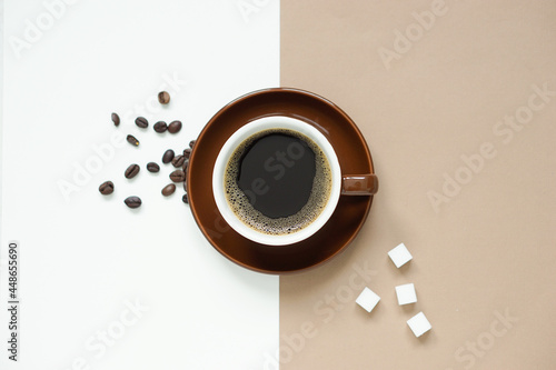 top view of black coffee in brown ceramic mug on brown ceramic plate placed on cream colour paper and brown paper,