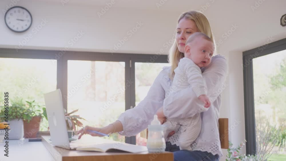 Working mother using laptop at home whilst looking after and cuddling baby son- shot in slow motion Working mother using laptop at home whilst looking after and cuddling baby son- shot in slow motion