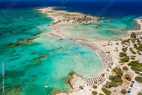 Fototapeta Naklejka Na Ścianę i Meble -  Aerial view of sunshades and umbrellas on a narrow sandy beach surrounded by shallow lagoons (Elafonisso Beach, Crete, Greece)