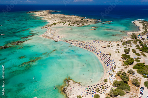 Aerial view of sunshades and umbrellas on a narrow sandy beach surrounded by shallow lagoons (Elafonisso Beach, Crete, Greece)