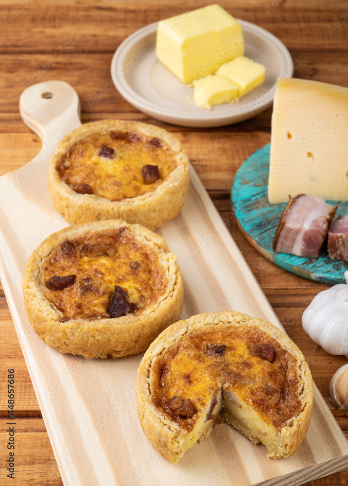 Homemade quiche lorraine over wooden board with ingredients