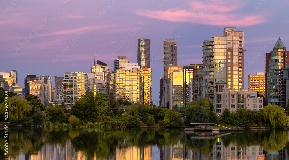 View of Lost Lagoon in famous Stanley Park in a modern city with buildings skyline in background. Colorful Sunset Sky. Downtown Vancouver, BC, Canada.