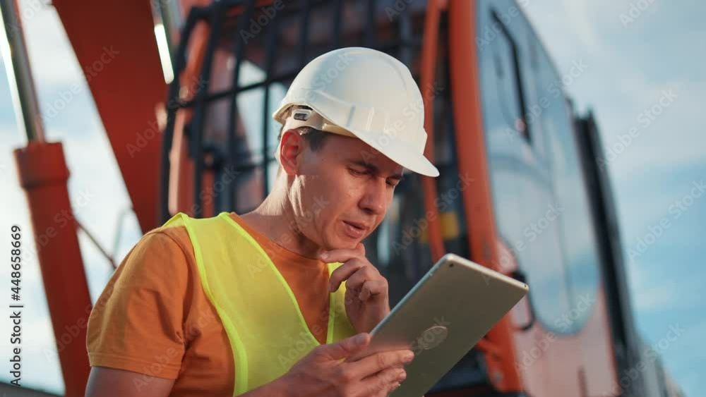 worker in hard a hat with digital tablet near excavator. construction site business driver with online digital tablet. industry construction concept. worker hard hat near excavator truck in uniform. worker in hard a hat with digital tablet near excavator. construction site business driver with online digital tablet. industry construction concept. worker hard hat near excavator truck in uniform.