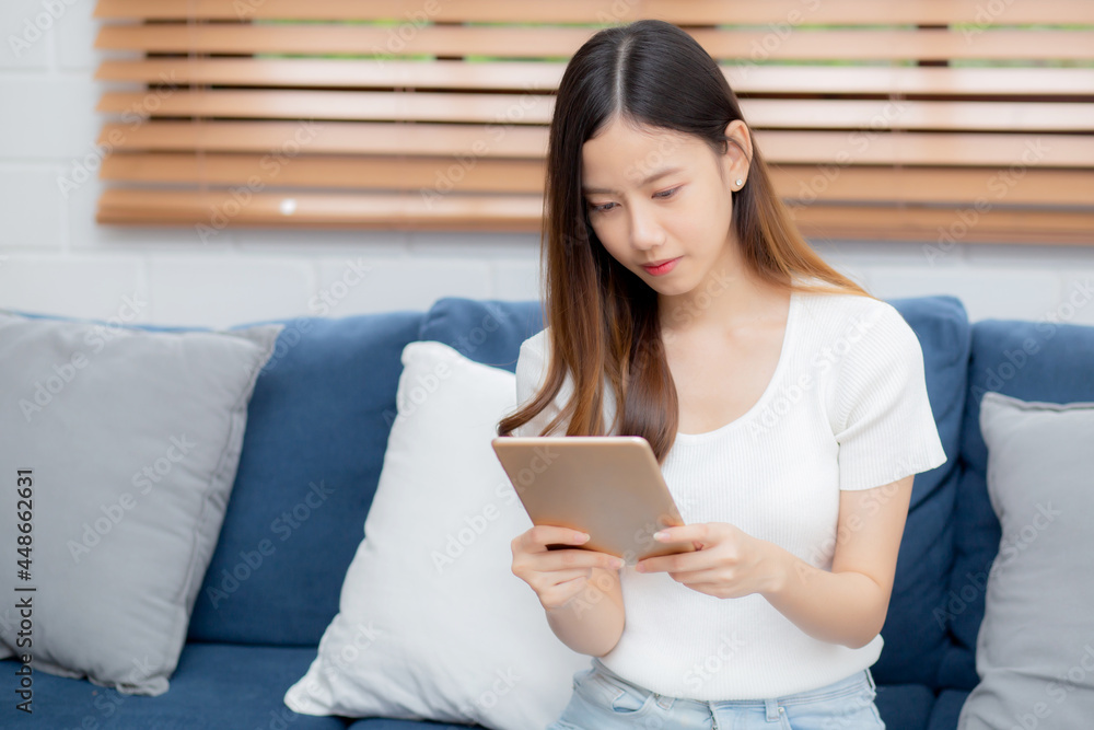 Young attractive asian woman resting using browsing tablet computer on sofa at home, happy girl sitting on couch relax reading digital gadget at house, communication and lifestyle concept. Young attractive asian woman resting using browsing tablet computer on sofa at home, happy girl sitting on couch relax reading digital gadget at house, communication and lifestyle concept.