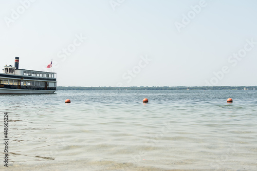 Tourist boat on the water at a lake in the Midwest USA; calm water with buoys on a line to mark off swimming area in foreground