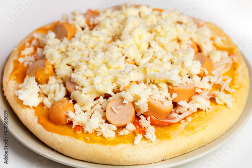 Pizza with mozzarella cheese, crab sticks, sausages and sauce, placed in a gray plate during preparation before being put into the oven, Cooking homemade