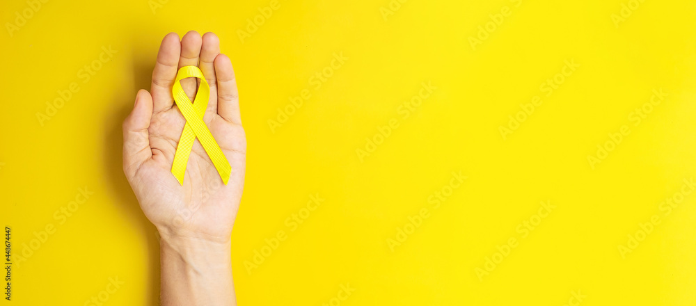hand holding Yellow Ribbon on yellow background for supporting people living and illness. September Suicide prevention day, Childhood Cancer Awareness month and World cancer day concept