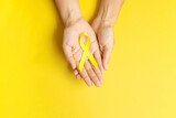 hand holding Yellow Ribbon on yellow background for supporting people living and illness. September Suicide prevention day, Childhood Cancer Awareness month and World cancer day concept