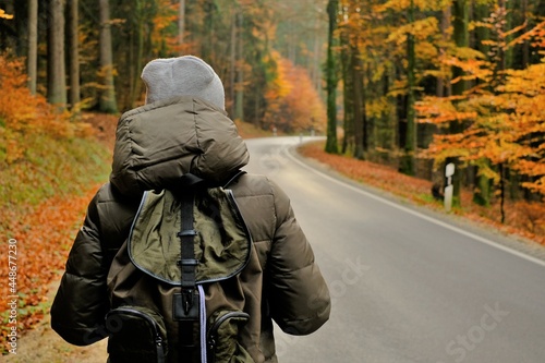 Traveler with a backpack.Hitchhiking travel. Autumn hikes and travel. Girl with a backpack walks along the road in the autumn forest. Walk and sport in the autumn season.