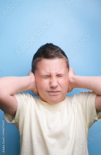 boy covering ears with hand being tired, headache, showing true emotion. Not listened.Closed ears