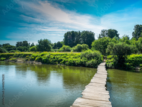 Ilillian summer landscape with river and forest, wooden boardwalk across the river