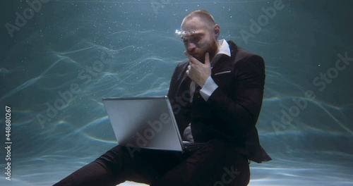 Creative occupation concept. Young happy businessman in suit thinking, using laptop to work under water slow motion. photo