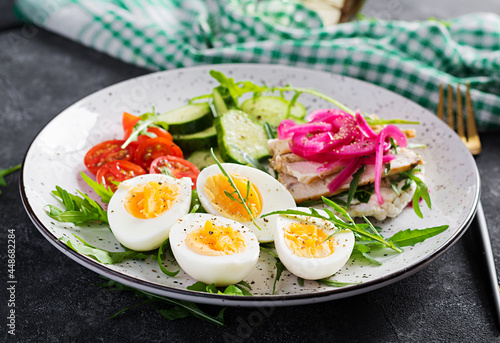 Breakfast. Boiled eggs salad with greens, cucumbers, tomato and sandwich with ricotta cheese, fried chicken fillet and red onion. Keto/paleo lunch.