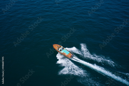 Top view of a wooden open large motor boat. Luxurious wooden boat fast movement on dark water. Classic Italian wooden boat fast moving aerial view.