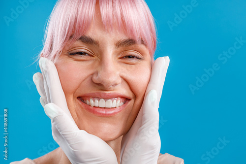 Close up shot of happy smiling woman. Hands of beautician examining female face before giving facial botox injections. Beauty concept