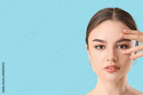 Beautiful young woman massaging her face on color background