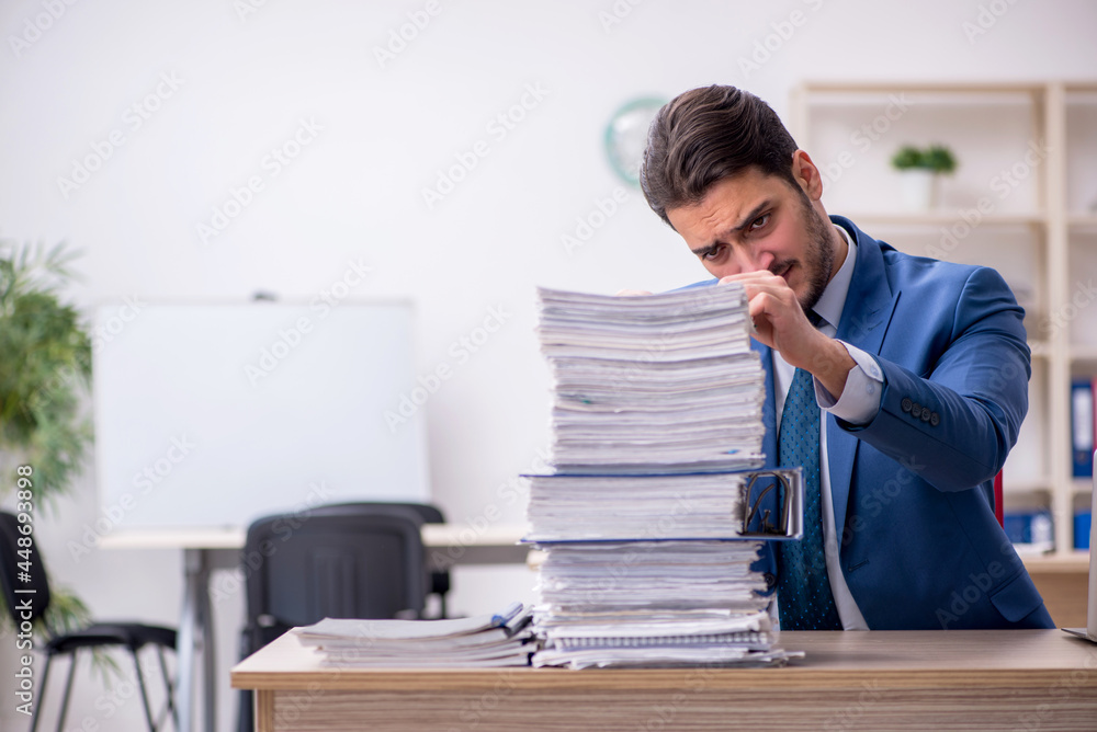 Naklejka premium Young businessman employee and too much work in the office