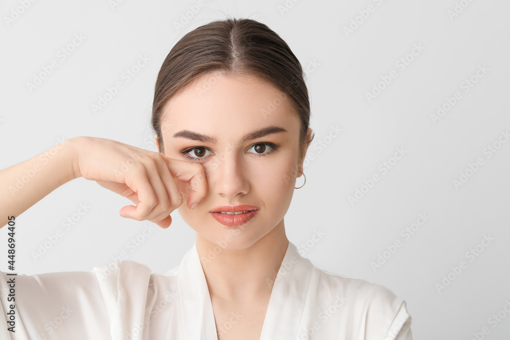 Beautiful young woman massaging her face on light background Beautiful young woman massaging her face on light background