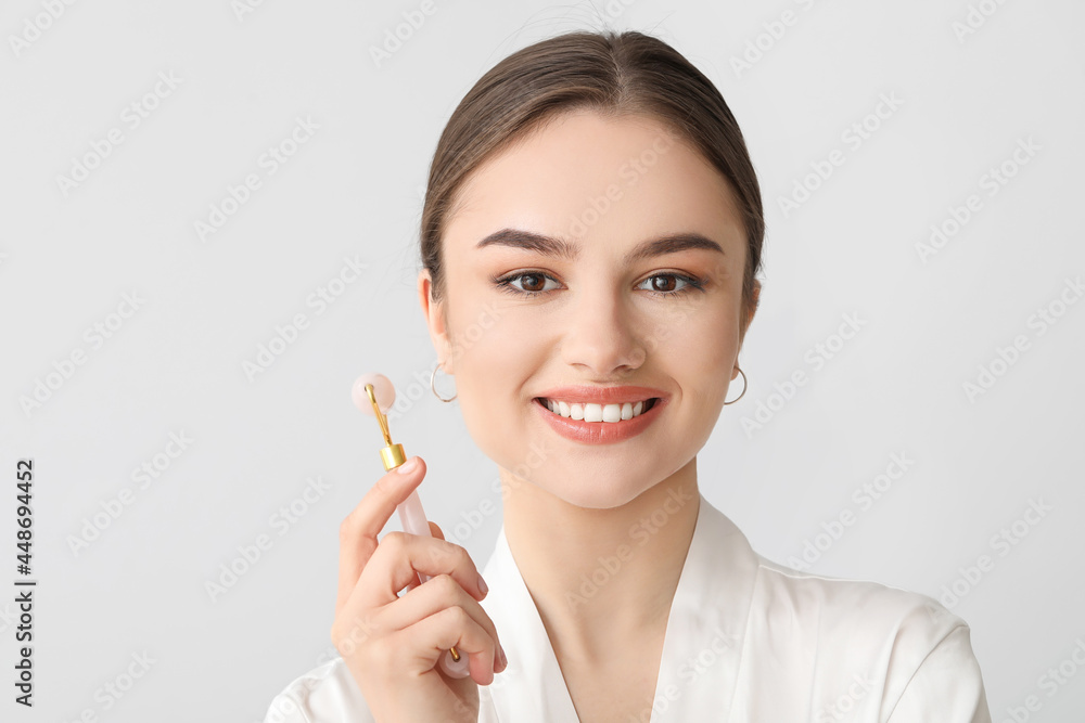 Beautiful young woman with facial massage tool on light background Beautiful young woman with facial massage tool on light background