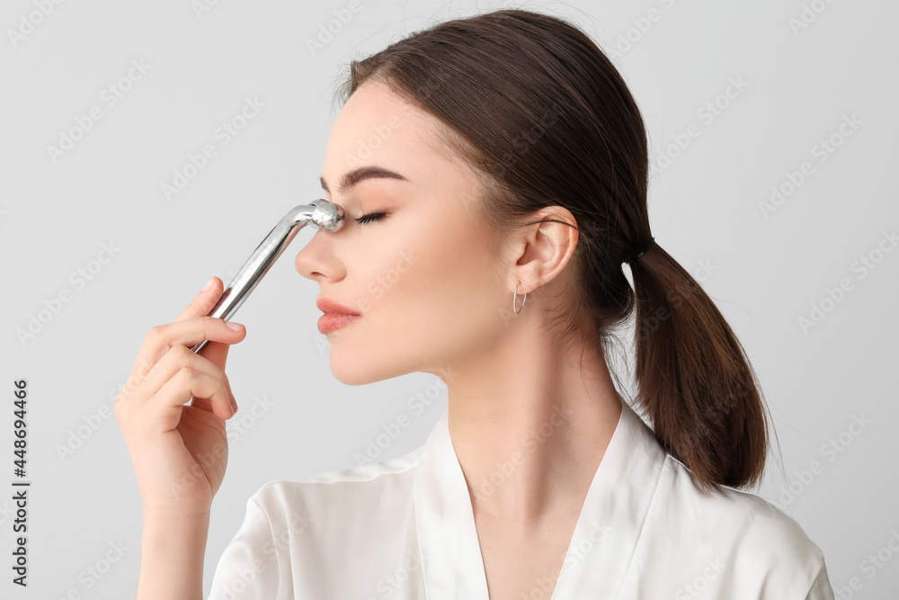 Beautiful young woman with facial massage tool on light background Beautiful young woman with facial massage tool on light background
