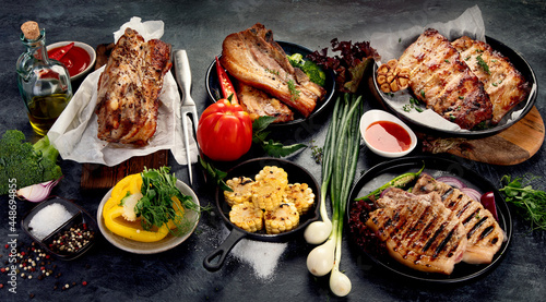 Assortment of grilled pork meat with vegetables on dark grey background.