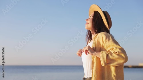 Side view profile happy traveler tourist young brunette woman 20s eyes closed wears summer casual clothes straw hat stand at sand shore breathe deeple stretch isolated on sea beach background outdoors photo