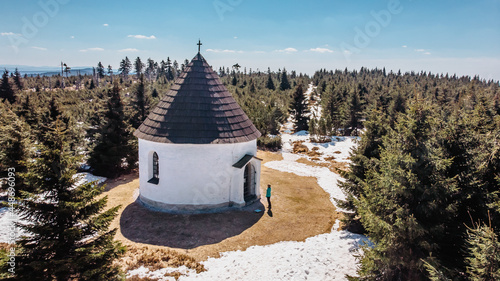 Aerial view of baroque Chapel of the Visitation of Virgin Mary,Kunstat Chapel, located in Eagle Mountains,Czech Republic.Circular floor plan and roof covered with shingles.Female traveler in winter. photo