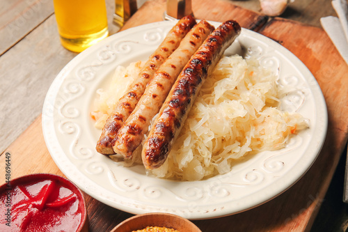 Plate with tasty grilled sausages and sauerkraut on wooden background, closeup