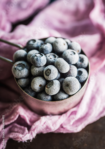 Frozen blueberries in metal cup on the rustic background. Selective focus.