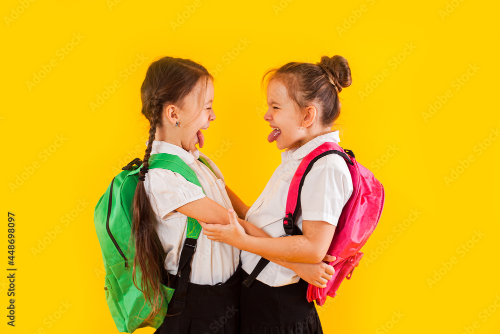 Two smiling schoolgirls in uniform are hugging at the yellow