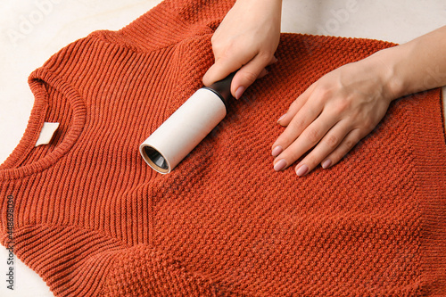 Woman cleaning sweater with lint roller on light background, closeup