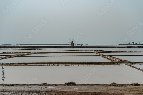 Saline of the Laguna Marsala,Sicily,Italy.Nature reserve with beautiful windmills,brine pools shimmering with different colors,traditional production method of sea salt.Salt flats in cloudy summer day
