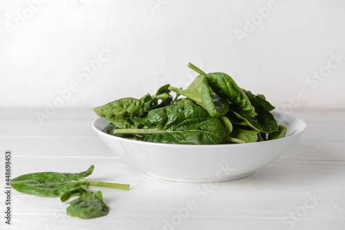 Bowl with fresh spinach leaves on light wooden background