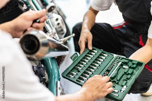 Two professional automotive technician worker choosing screwdriver for repair motorcycle in automobile repair service shop. Selective focus on tool box.
