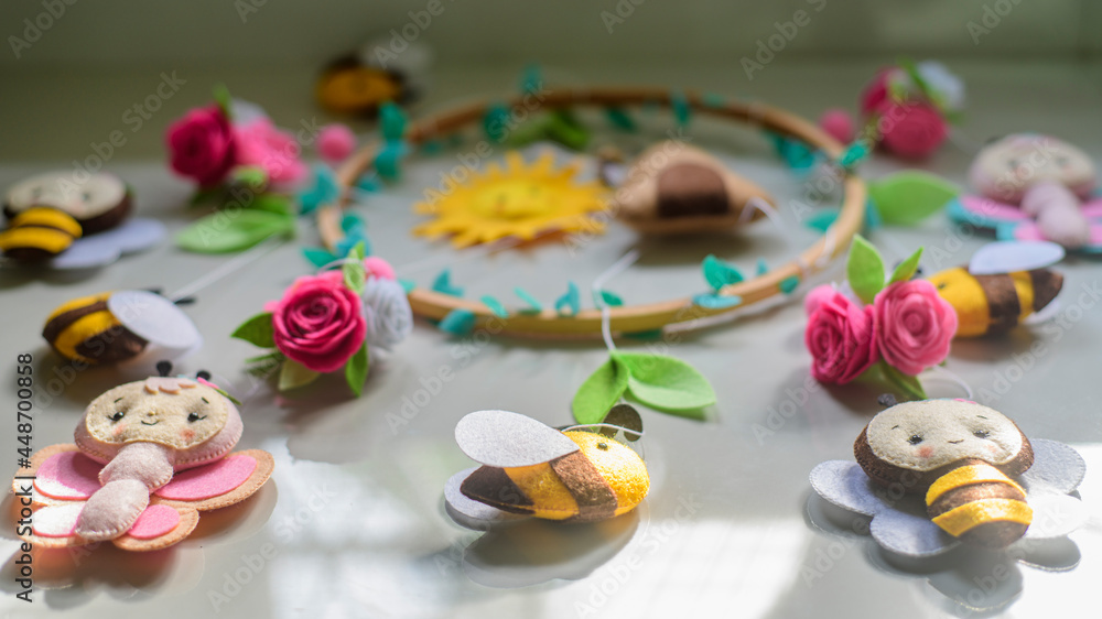 Beautiful cot mobile laid out on a tiled floor, stuffed cute bees and flowers attached to the embroidery hoop cot mobile.