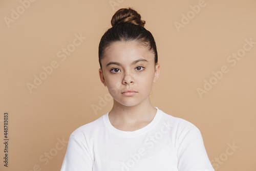 Serious teenage girl with a bundle of hair looks at the camera. Cute little girl on a pink background