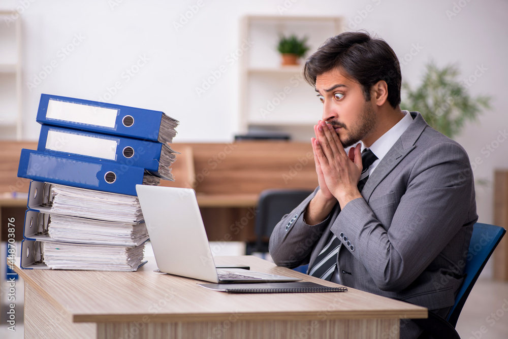 Young male employee unhappy with excessive work in the office Young male employee unhappy with excessive work in the office