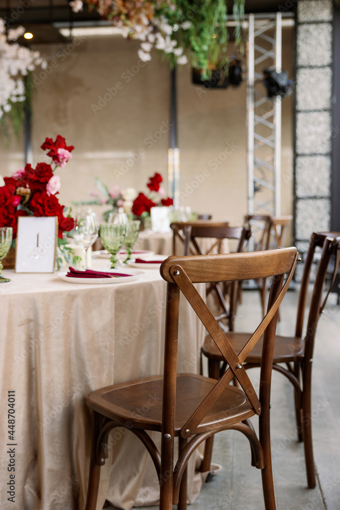 Decoration of the wedding table with red and pink flowers on a white tablecloth. Red glass goblets and burgundy napkins on the plates. Decoration of the wedding table with red and pink flowers on a white tablecloth. Red glass goblets and burgundy napkins on the plates.