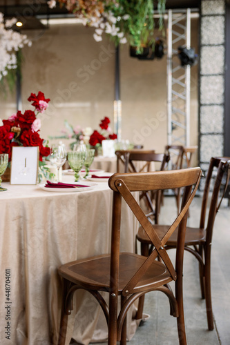 Decoration of the wedding table with red and pink flowers on a white tablecloth. Red glass goblets and burgundy napkins on the plates. photo