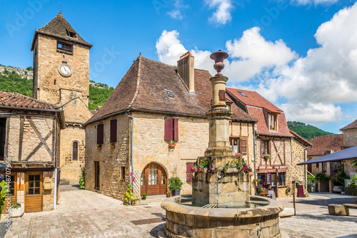 Fototapeta Naklejka Na Ścianę i Meble -  View at the Fountain and Bell tower of Church of Saint Pierre from Main sqaure of Autoire village - France